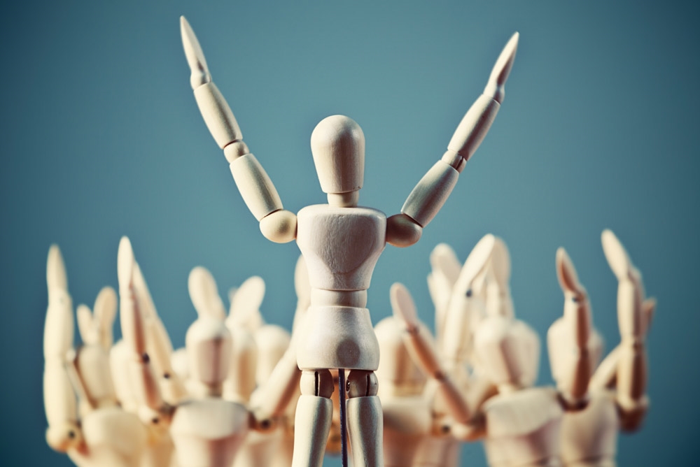 Artist mannequin with hands raised in air inciting a group of mannequins