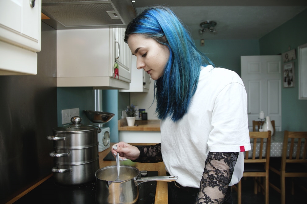 alternative teenager with blue hair in the kitchen cooking food