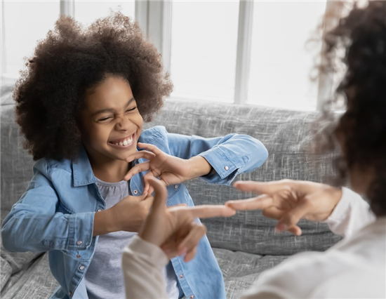 african-deaf-kid-girl-and-her-mother-sitting-on-couch-showing-symbols-with-hands